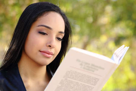 Close up of a beautiful woman reading a book in a park with a green unfocused backgroundの写真素材