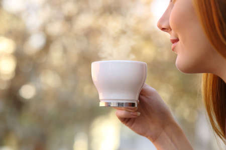 Close up of a woman holding a coffee cup with a blur warm backgroundの写真素材