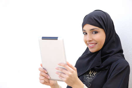 Arab woman holding a tablet and looking at camera on a white wall background        の写真素材