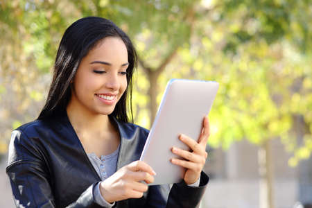 Happy woman reading a tablet reader in a park with a green background        