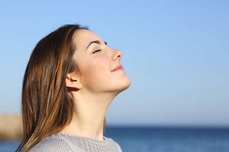 Woman profile portrait breathing deep fresh air on the beach with the ocean in the backgroundの写真素材