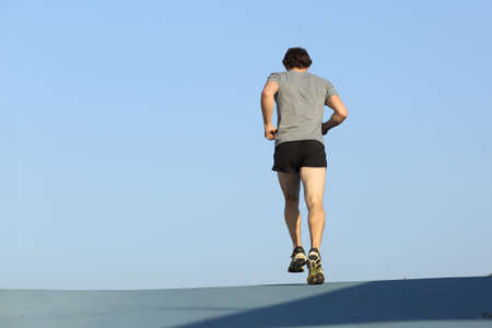 Back view of a jogger man running against blue sky with copy space 