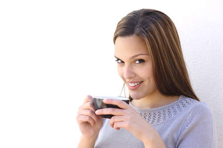 Relaxed woman holding a cup of coffee and looking at camera on a white wall             の写真素材