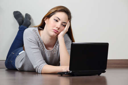Bored teenager girl browsing social media in a laptop lying on the floor at homeの写真素材