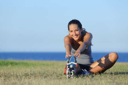 Fitness runner woman stretching on the grass with the sea and horizon in the backgroundの写真素材