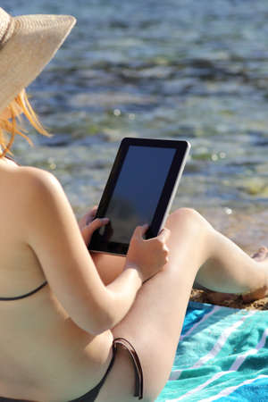 Back view of a woman reading a tablet on vacations on the beachの写真素材