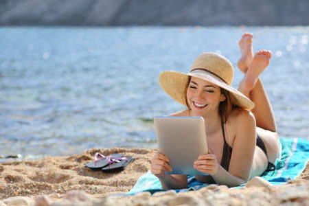 Pretty woman reading a tablet reader on the beach on vacations with the sea in the background               の写真素材