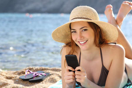 Woman texting in a smart phone on holidays on the beach with the sea in the background              の写真素材