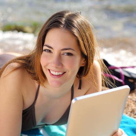 Portrait of a pretty happy woman using a tablet on the beach with the water in the backgroundの写真素材