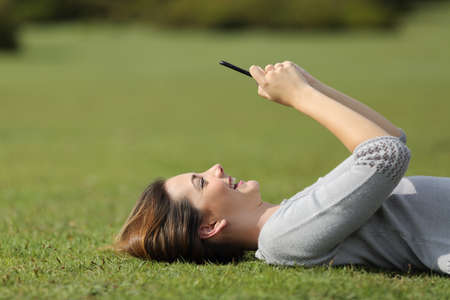 Woman using a smart phone resting on the grass in a park with an unfocused backgroundの写真素材