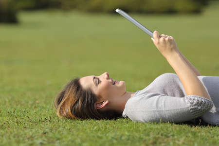 Profile of a happy woman reading a tablet reader on the grass of a park