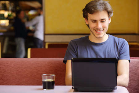 Happy relaxed man browsing social media surfing internet on a laptop in a restaurant           の写真素材