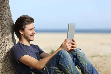 Happy man reading a tablet reader sitting on the beach with the horizon in the backgroundの写真素材