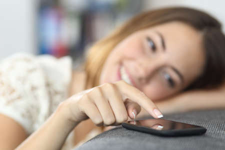Close up of a woman hand touching a smart phone sitting on a couch at home      の写真素材