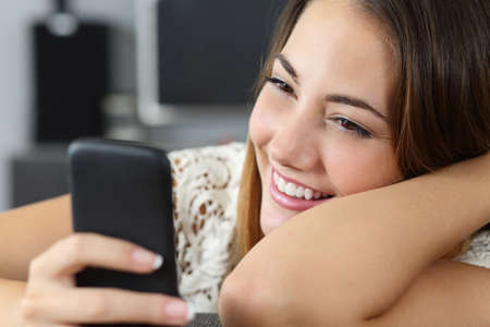 Funny woman using a smart phone at home on a couch texting and smilingの写真素材