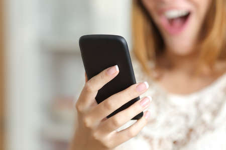 Close up of a surprised woman hand holding and using a smart phone at home            の写真素材