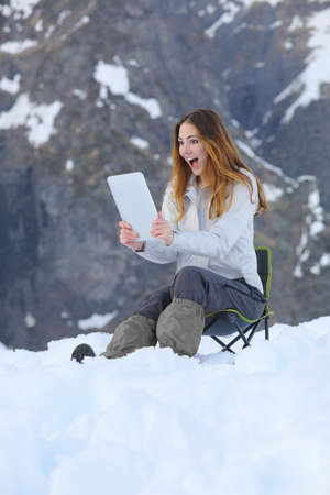 Amazed wow woman looking a tablet application in a snowy mountain on vacations              の写真素材