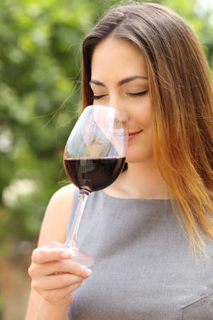 Somelier woman smelling and tasting red wine with a green background             の写真素材