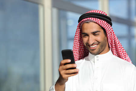 Arab saudi businessman working  with his phone with an office building in the backgroundの写真素材
