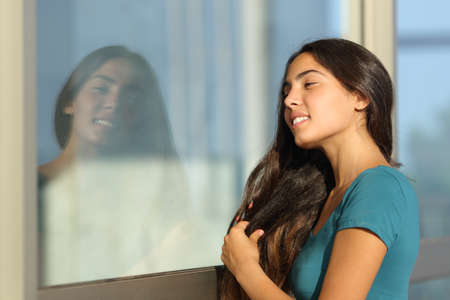 Flirty teen girl combing her hair using a window like a mirror outdoor in the streetの写真素材