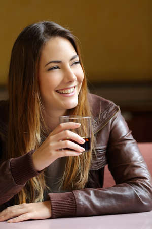 Happy woman thinking and holding a refreshment in a restaurant           の写真素材