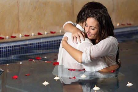 Romantic couple hugging in a pool  with candles and rose petals floating on the water
