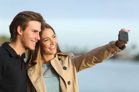 Happy couple photographing a selfie with the smart phone outdoors in winterの写真素材