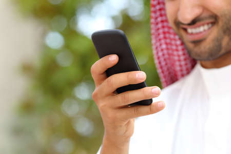Smiling arab saudi man hand using a smart phone outdoor in a park with a green backgroundの写真素材