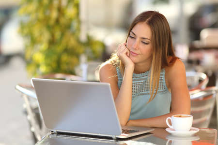 Serious woman watching a laptop in a restaurant terrace with an unfocused backgroundの写真素材