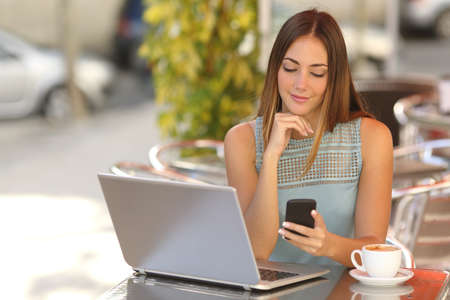 Self employed woman working with her phone and laptop in a restaurant terrace with a cup of coffeeの写真素材