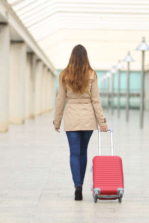 Back view of a tourist woman walking and carrying a suit case in an airport or stationの写真素材