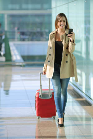 Front view of a traveler woman walking and using a smart phone in an airport corridorの写真素材