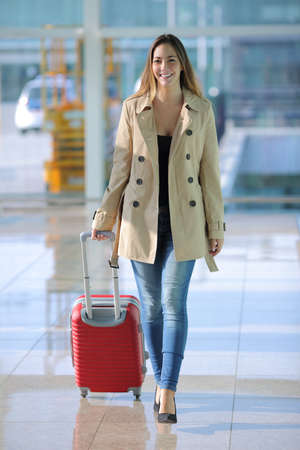 Front view of a traveler woman walking carrying a suitcase in an airport corridorの写真素材