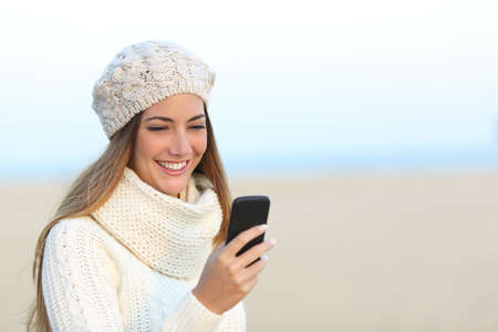 Woman warmly clothed in winter using a smart phone on the beachの写真素材