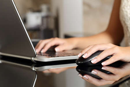 Close up of a woman hands working with a laptop and a mouse in a home interior or an office
