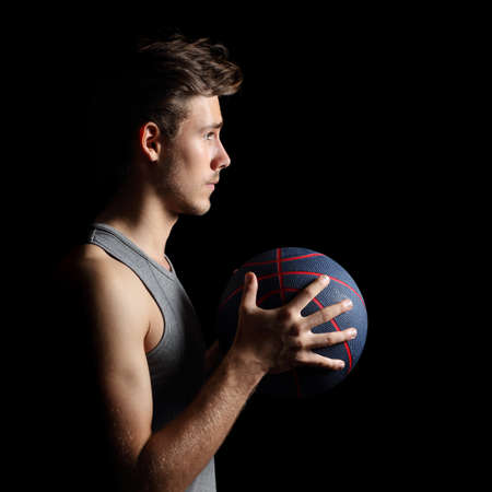 Side view of a basketball player holding a basket ball isolated on a black backgroundの写真素材