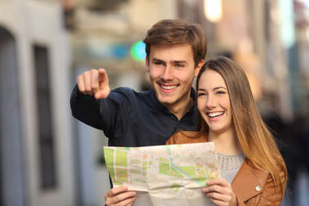 Happy couple of tourists on vacations searching a street in a map and pointing awayの写真素材