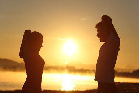 Silhouette of a fitness couple stretching at sunrise with the sun in the backgroundの写真素材