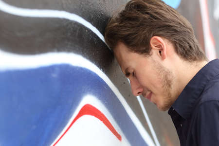 Depressed sad teenager boy lamenting with his head against a wall outdoorsの写真素材
