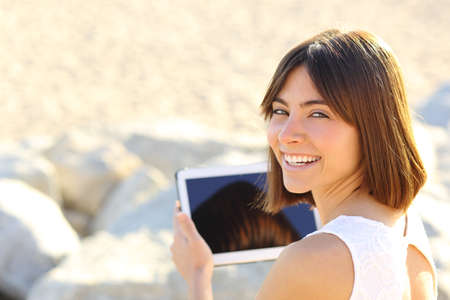 Happy woman using a tablet and looking at camera outdoorsの写真素材