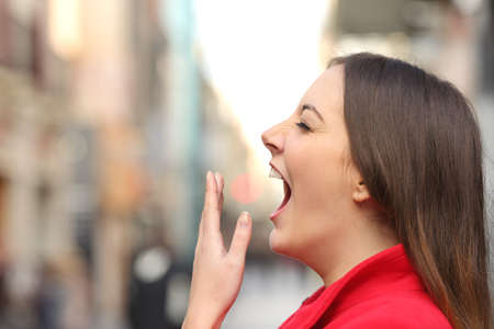Tired woman yawning in the street in the morning with an unfocused urban background