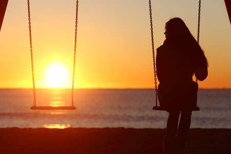 Single woman alone swinging on the beach and looking the other seat missing a boyfriendの写真素材