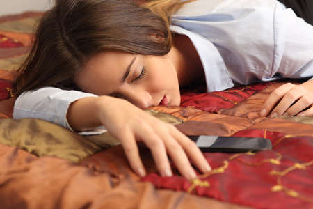 Close up portrait of a business woman tired and sleeping in an hotel bed with a mobile phone