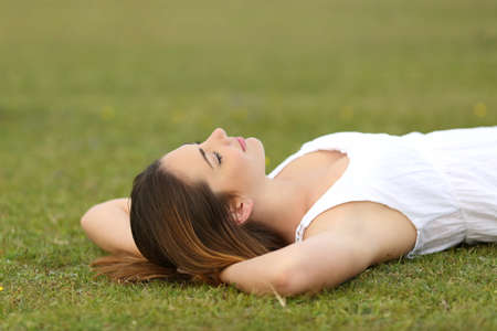 Relaxed woman lying on the grass sleeping in a tranquil scene with a green backgroundの写真素材