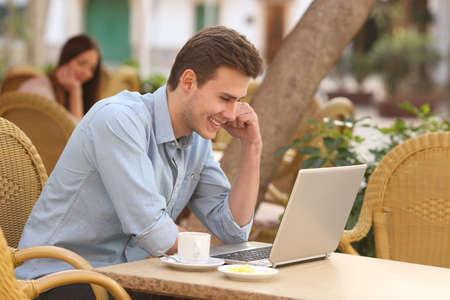 Happy man watching social media in a laptop in a restaurant terraceの写真素材