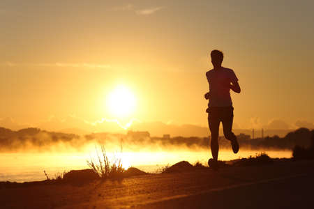 Silhouette of a man running at sunrise with the sun in the backgroundの写真素材
