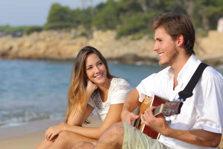 Man flirting playing guitar while a girl looks him amazed with the sea in the backgroundの写真素材