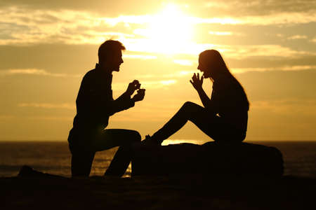 Proposal on the beach with a man silhouette asking for marry at sunset with the sun in the backgroundの写真素材