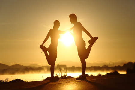 Silhouette of a fitness couple profile stretching at sunset with the sun in the backgroundの写真素材