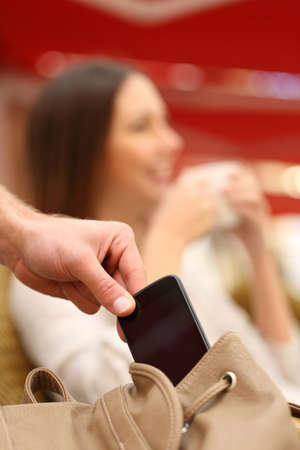 Thief hand stealing a mobile phone from a woman bag while she is relaxedの写真素材